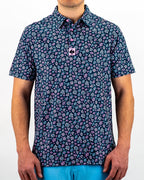 Men’s Daisy Daze golf polo by Pins & Aces featuring an all-over pink, blue, and white daisy floral print on a navy background with an athletic performance fit.