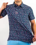 Men’s Daisy Daze golf polo by Pins & Aces featuring an all-over pink, blue, and white daisy floral print on a navy background with an athletic performance fit.