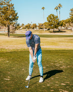 Men’s Daisy Daze golf polo by Pins & Aces featuring an all-over pink, blue, and white daisy floral print on a navy background with an athletic performance fit.