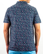 Men’s Daisy Daze golf polo by Pins & Aces featuring an all-over pink, blue, and white daisy floral print on a navy background with an athletic performance fit.