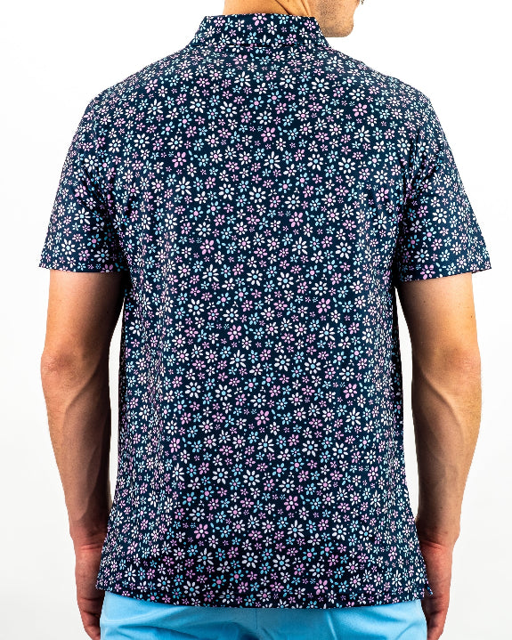 Men’s Daisy Daze golf polo by Pins & Aces featuring an all-over pink, blue, and white daisy floral print on a navy background with an athletic performance fit.