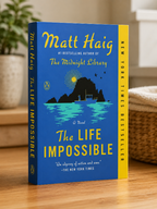 "The Life Impossible by Matt Haig paperback fiction novel featuring a small boat on blue water beneath a moonlit island and starry night sky."