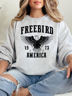 Women’s Freebird 1973 graphic tee featuring a bold Freebird America design, bald eagle graphic, black detailing, and vintage-inspired artwork on a Comfort Colors® cotton Crewneck in Grey