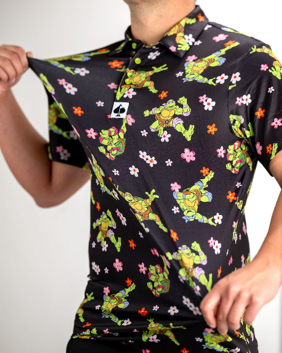 Black TMNT Turtle Flower Power golf polo by Pins & Aces featuring colorful Teenage Mutant Ninja Turtles characters and floral print.