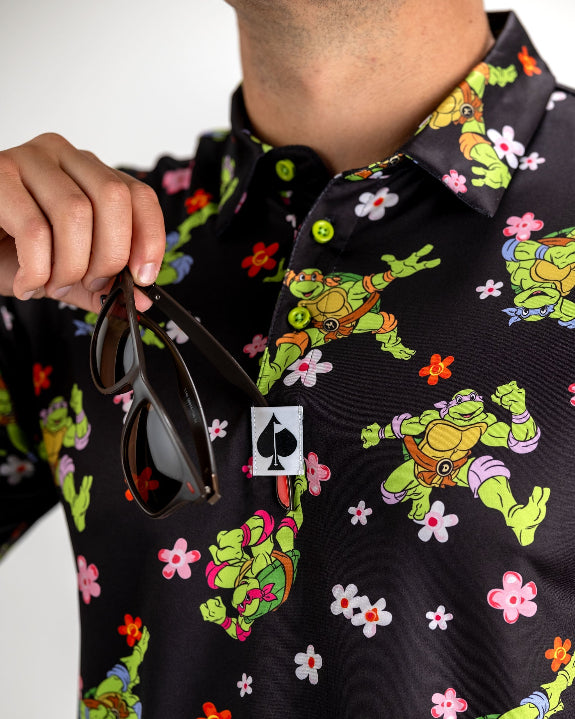 Black TMNT Turtle Flower Power golf polo by Pins & Aces featuring colorful Teenage Mutant Ninja Turtles characters and floral print.