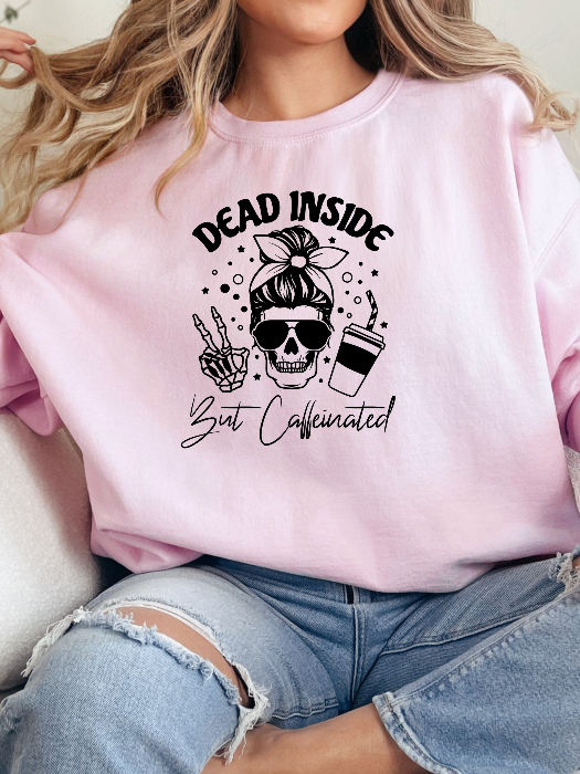 Dead Inside But Caffeinated graphic available as a tee, crewneck, or sweatshirt featuring a fun coffee-inspired design on soft cotton-blend fabric, perfect for Halloween, spooky season, and everyday fall outfits. Crewneck in light pink
