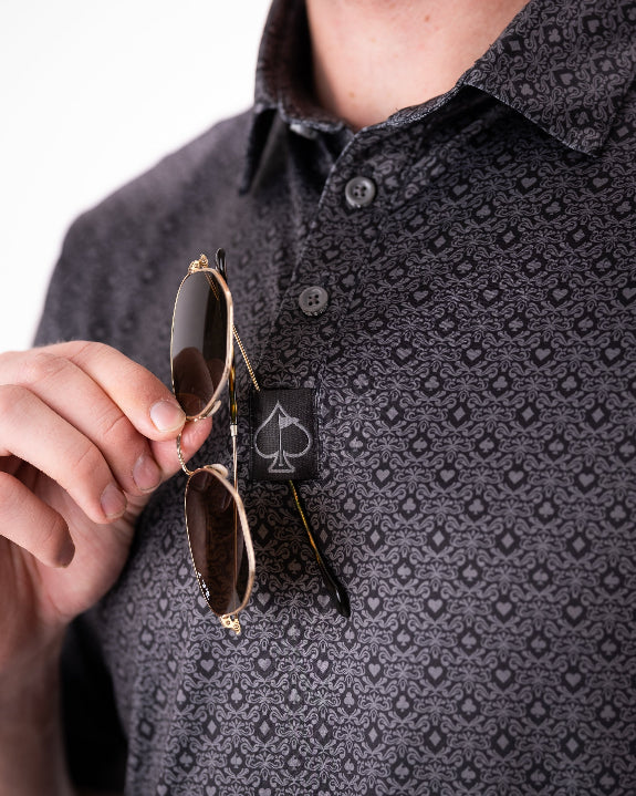Men’s Big Blind golf polo by Pins & Aces featuring a subtle dark gray and black geometric pattern with short sleeves, collared neckline, and athletic fit.