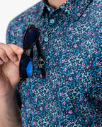 Men’s Fluorescent Floral golf polo by Pins & Aces featuring a vibrant pink, teal, and blue floral pattern on a dark navy short-sleeve performance shirt.