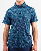Men’s Fluorescent Floral golf polo by Pins & Aces featuring a vibrant pink, teal, and blue floral pattern on a dark navy short-sleeve performance shirt.