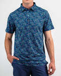 Men’s Fluorescent Floral golf polo by Pins & Aces featuring a vibrant pink, teal, and blue floral pattern on a dark navy short-sleeve performance shirt.