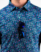 Men’s Fluorescent Floral golf polo by Pins & Aces featuring a vibrant pink, teal, and blue floral pattern on a dark navy short-sleeve performance shirt.