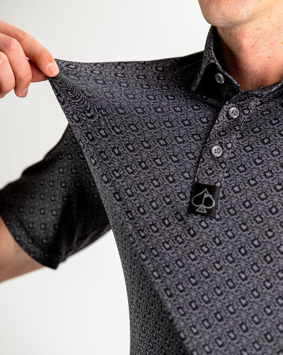 Men’s Big Blind golf polo by Pins & Aces featuring a subtle dark gray and black geometric pattern with short sleeves, collared neckline, and athletic fit.