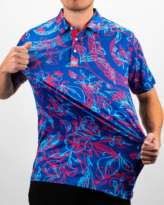 Men’s Cabo Colada golf polo by Pins & Aces featuring a vibrant coral red and aqua tropical floral print on a rich blue background with short sleeves and an athletic performance fit.