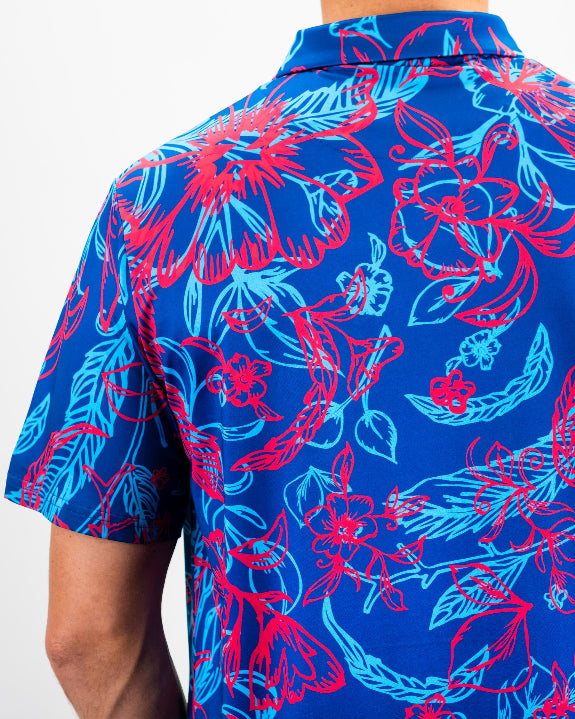 Men’s Cabo Colada golf polo by Pins & Aces featuring a vibrant coral red and aqua tropical floral print on a rich blue background with short sleeves and an athletic performance fit.
