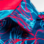 Men’s Cabo Colada golf polo by Pins & Aces featuring a vibrant coral red and aqua tropical floral print on a rich blue background with short sleeves and an athletic performance fit.
