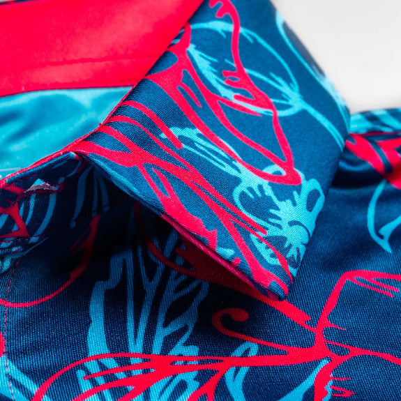 Men’s Cabo Colada golf polo by Pins & Aces featuring a vibrant coral red and aqua tropical floral print on a rich blue background with short sleeves and an athletic performance fit.