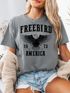Women’s Freebird 1973 graphic tee featuring a bold Freebird America design, bald eagle graphic, black detailing, and vintage-inspired artwork on a Comfort Colors® cotton T-shirt in Grey