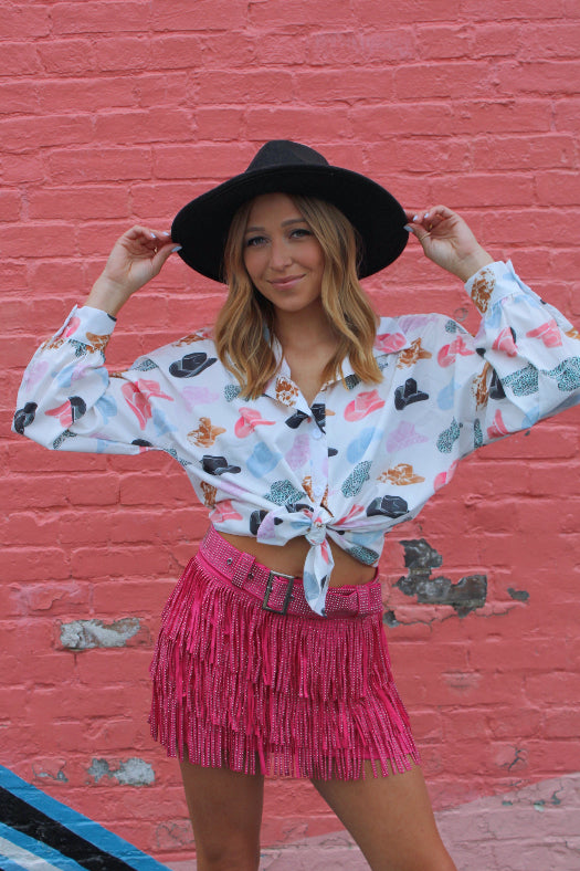 Women’s Nashville Babe pink Western mini skirt featuring triple-layer rhinestone fringe, a high-rise fit, matching belt, and built-in shorts.