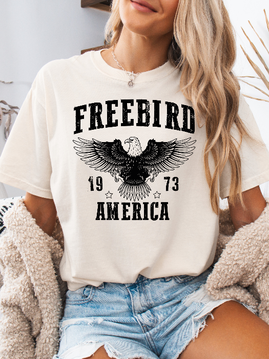 Women’s Freebird 1973 graphic tee featuring a bold Freebird America design, bald eagle graphic, black detailing, and vintage-inspired artwork on a Comfort Colors® cotton T-shirt in Ivory