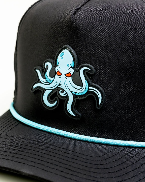 Kraken Black perforated rope golf hat by Pins & Aces featuring an all-black design, braided rope accent, breathable perforated panels, adjustable snapback, and built-in magnetic golf ball marker holder.