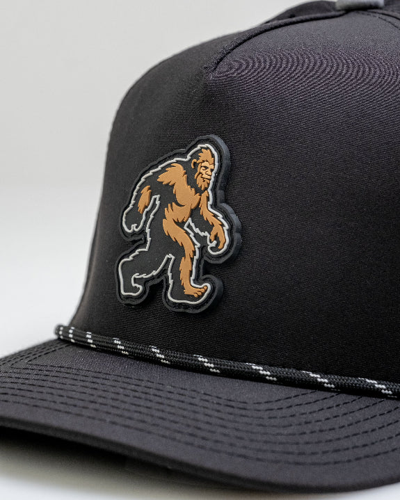 Pins & Aces Sasquatch Black perforated golf rope hat with adjustable snapback, magnetic ball marker holder, and matching golf ball marker.