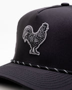 Black Pins & Aces perforated rope golf hat featuring an embroidered rooster on the front, breathable side panels, rope detail, and adjustable snapback design.