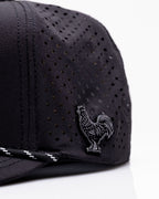 Black Pins & Aces perforated rope golf hat featuring an embroidered rooster on the front, breathable side panels, rope detail, and adjustable snapback design.