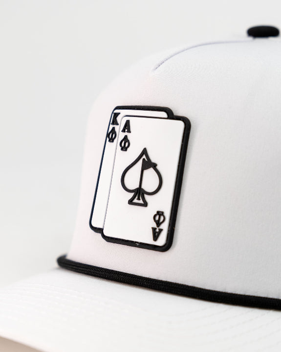 Ace/King White perforated rope golf hat by Pins & Aces with an adjustable snapback, built-in magnetic ball marker holder, and matching golf ball marker.