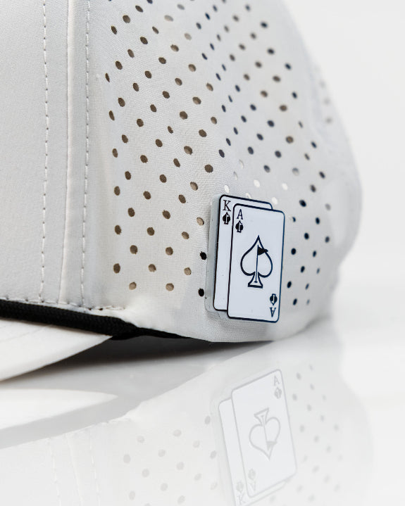 Ace/King White perforated rope golf hat by Pins & Aces with an adjustable snapback, built-in magnetic ball marker holder, and matching golf ball marker.