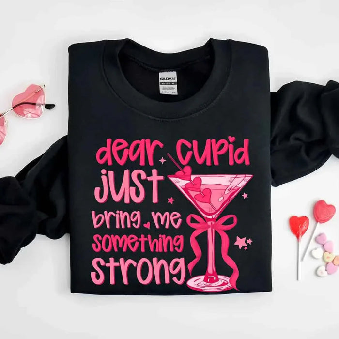 Dear Cupid Something Strong Valentine’s Day crewneck sweatshirt featuring a funny Cupid-inspired graphic on a cozy relaxed-fit unisex sweatshirt in Black