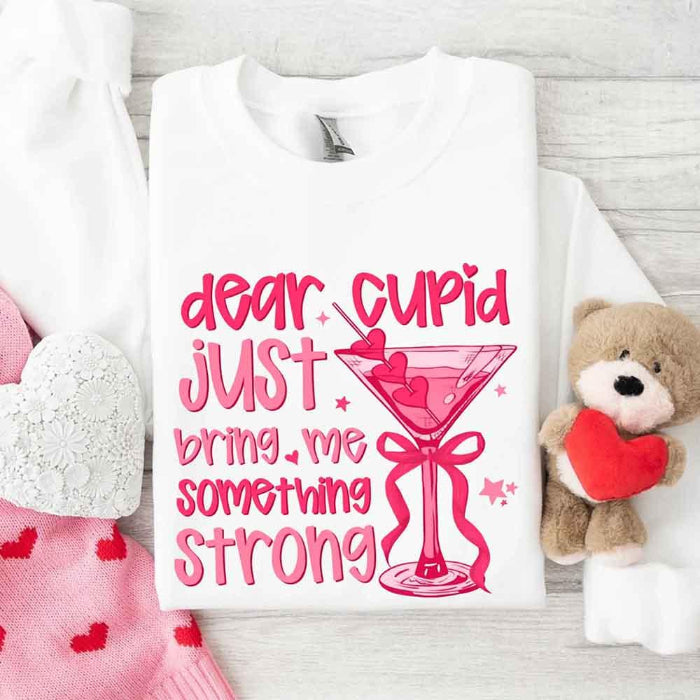 Dear Cupid Something Strong Valentine’s Day crewneck sweatshirt featuring a funny Cupid-inspired graphic on a cozy relaxed-fit unisex sweatshirt in White