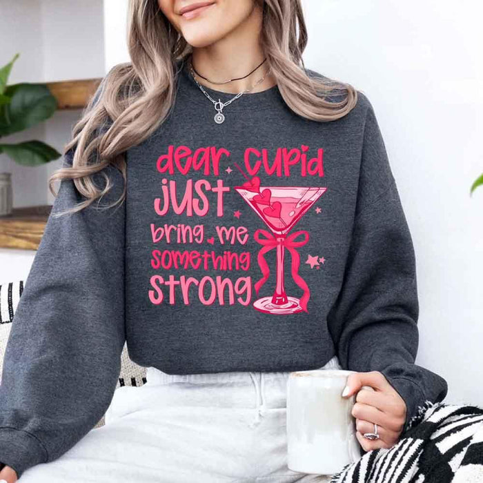 Dear Cupid Something Strong Valentine’s Day crewneck sweatshirt featuring a funny Cupid-inspired graphic on a cozy relaxed-fit unisex sweatshirt in Dark Heather