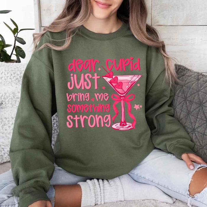 Dear Cupid Something Strong Valentine’s Day crewneck sweatshirt featuring a funny Cupid-inspired graphic on a cozy relaxed-fit unisex sweatshirt in Military Green