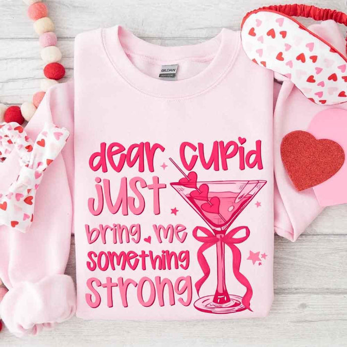 Dear Cupid Something Strong Valentine’s Day crewneck sweatshirt featuring a funny Cupid-inspired graphic on a cozy relaxed-fit unisex sweatshirt in Light Pink
