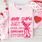 Dear Cupid Something Strong Valentine’s Day crewneck sweatshirt featuring a funny Cupid-inspired graphic on a cozy relaxed-fit unisex sweatshirt in Light Pink