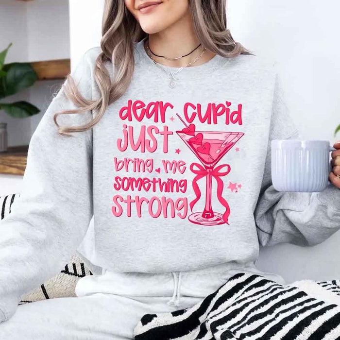 Dear Cupid Something Strong Valentine’s Day crewneck sweatshirt featuring a funny Cupid-inspired graphic on a cozy relaxed-fit unisex sweatshirt in Ash