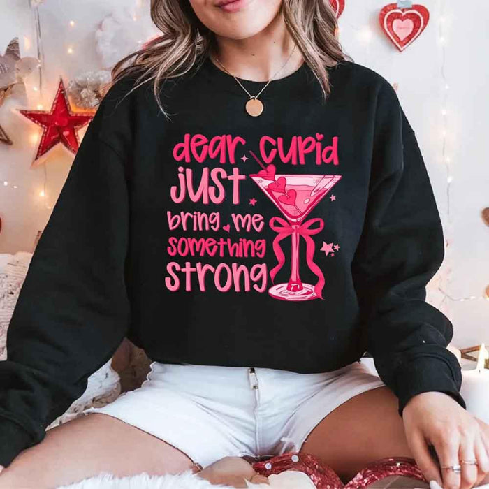 Dear Cupid Something Strong Valentine’s Day crewneck sweatshirt featuring a funny Cupid-inspired graphic on a cozy relaxed-fit unisex sweatshirt in Black