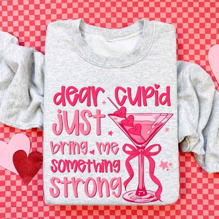 Dear Cupid Something Strong Valentine’s Day crewneck sweatshirt featuring a funny Cupid-inspired graphic on a cozy relaxed-fit unisex sweatshirt in Ash