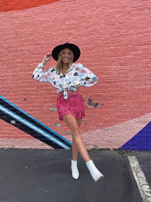 Women’s Nashville Babe pink Western mini skirt featuring triple-layer rhinestone fringe, a high-rise fit, matching belt, and built-in shorts.