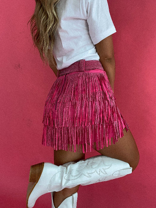 Women’s Nashville Babe pink Western mini skirt featuring triple-layer rhinestone fringe, a high-rise fit, matching belt, and built-in shorts.