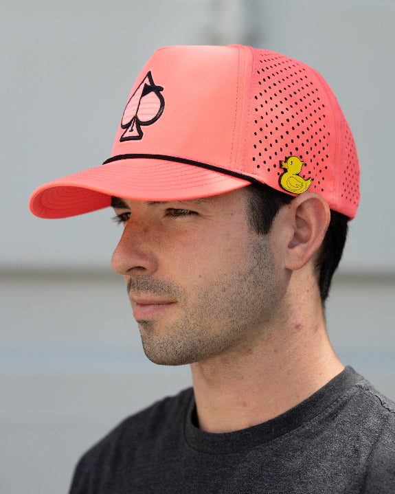 Highlighter pink perforated rope golf hat by Pins & Aces featuring an embroidered Fairway Wave Spade logo, adjustable snapback, and built-in magnetic golf ball marker holder.