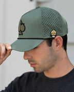 Olive green perforated rope golf hat by Pins & Aces featuring an embroidered Fairway Wave Spade logo, rope accent, adjustable snapback, and built-in magnetic golf ball marker holder.