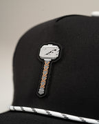 Thor’s Hammer Black perforated rope golf hat by Pins & Aces featuring a hammer-inspired design, adjustable snapback, breathable perforations, and built-in magnetic ball marker holder.