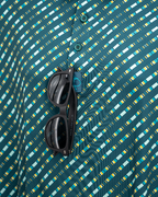 Men’s Chromo Green performance golf polo by Pins & Aces featuring an all-over green, blue, and yellow diagonal geometric stripe pattern with short sleeves and an athletic fit.