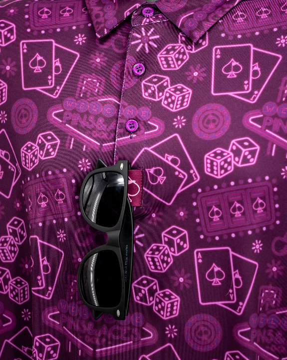 Men’s purple casino golf polo by Pins & Aces featuring an all-over pattern of playing cards, dice, poker chips, slot machines, and Las Vegas-inspired graphics.