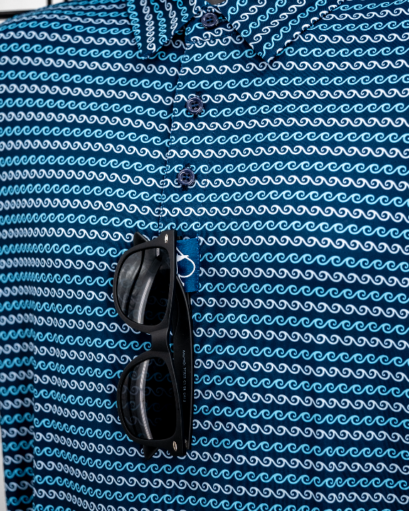Men’s Rising Tides golf polo by Pins & Aces featuring a repeating blue and navy wave-inspired pattern, short sleeves, and an athletic performance fit.