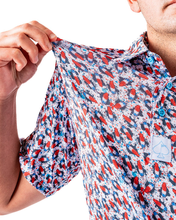 Men’s Bomb Pop Splatter golf polo by Pins & Aces featuring an all-over red, white, and blue splatter pattern with short sleeves and an athletic performance fit.