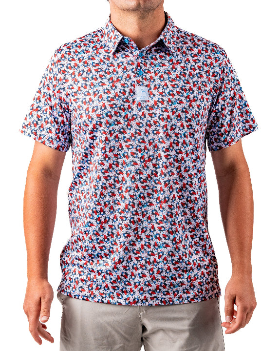 Men’s Bomb Pop Splatter golf polo by Pins & Aces featuring an all-over red, white, and blue splatter pattern with short sleeves and an athletic performance fit.