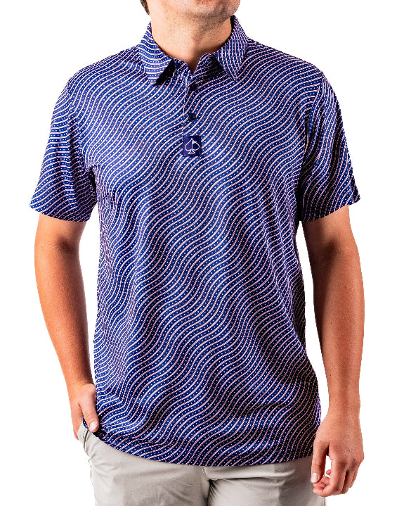 Men’s Wavy Stars & Stripes golf polo by Pins & Aces featuring a navy, red, and white wavy patriotic pattern with short sleeves and an athletic performance fit.