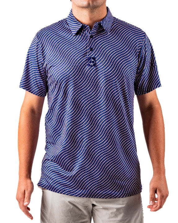 Men’s Wavy Stars & Stripes golf polo by Pins & Aces featuring a navy, red, and white wavy patriotic pattern with short sleeves and an athletic performance fit.